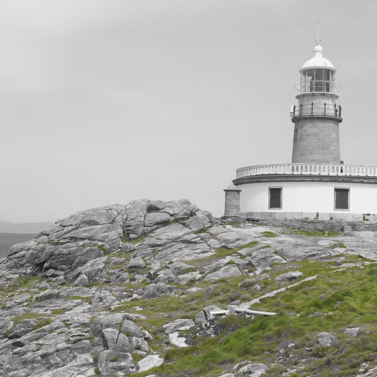 Faro blanco sobre costa rocosa, fotografía en blanco y negro
