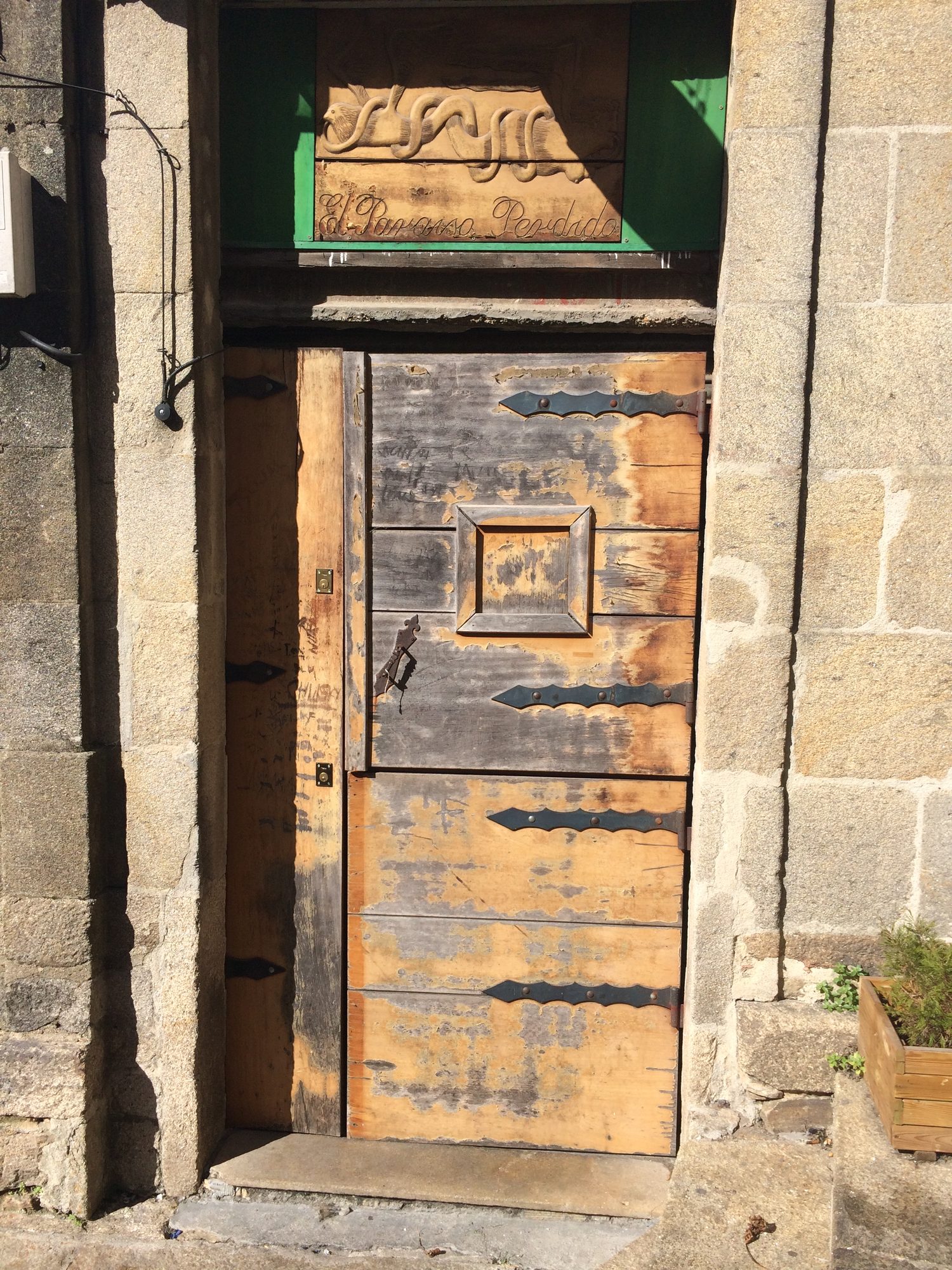 Puerta antigua de madera con herrajes de hierro y cartel tallado "El Paraíso Perdido"
