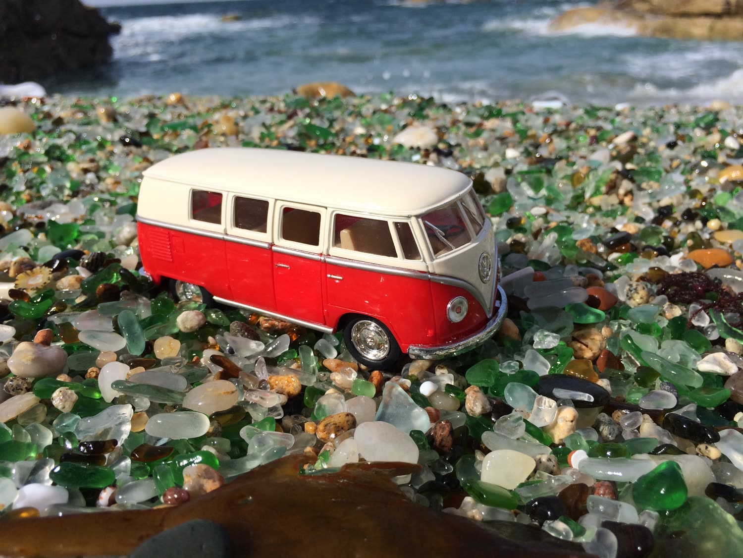 Combi Volkswagen en miniatura sobre una playa de vidrios de mar