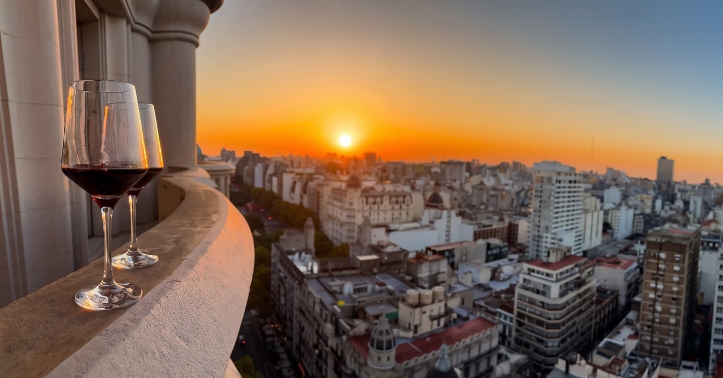 Copa de vino junto a una baranda con vista panorámica de la ciudad al atardecer