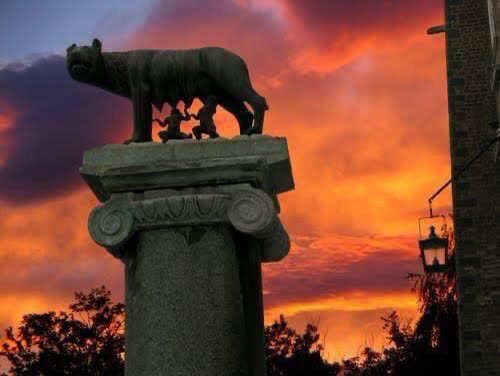 Estatua de la loba capitolina sobre una columna, cielo naranja de atardecer