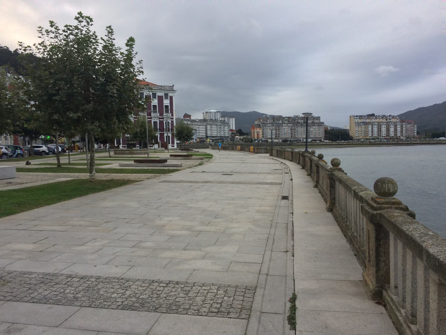 Paseo peatonal junto al agua con edificios de fondo, día nublado
