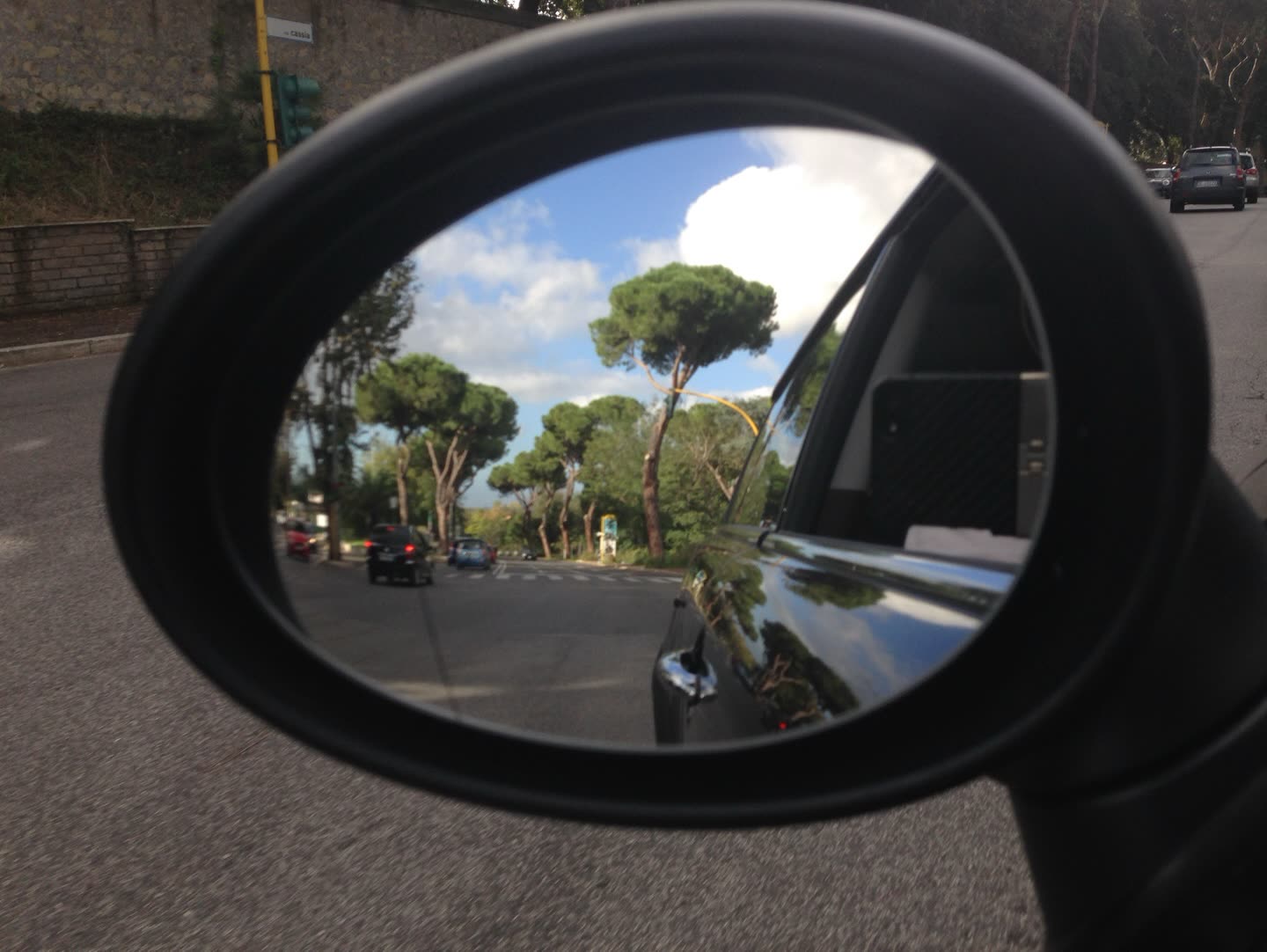 Reflejo de árboles y cielo en el espejo retrovisor de un auto